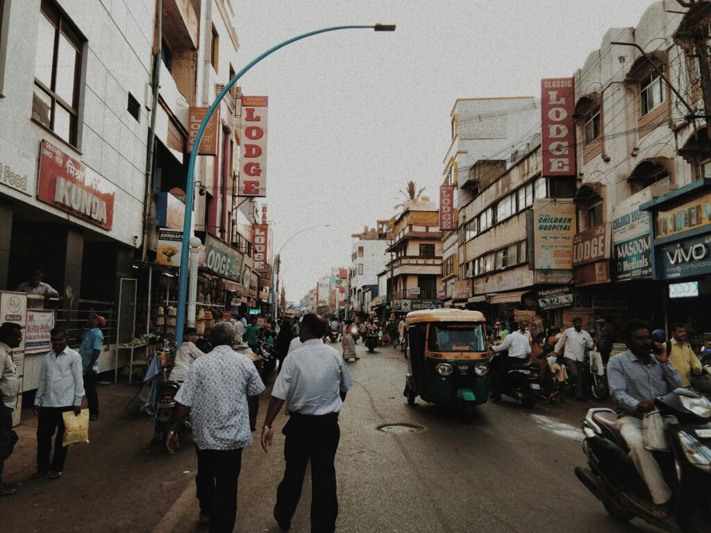 Lively street in Belgaum, India with people, shops, and vehicles in an urban setting.