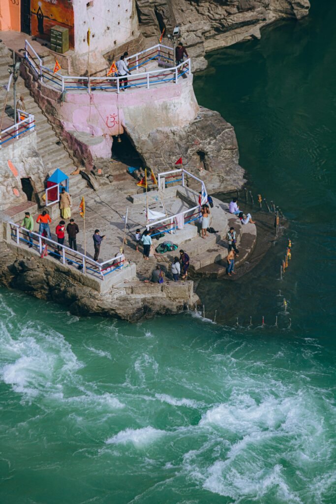 Aerial view of people performing rituals by the river in Rishikesh, India. The turquoise waters add a serene beauty.